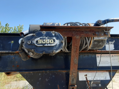 Winch motor and metal frame on a used Kaufman car hauler trailer showing a rusted winch and coiled cable.