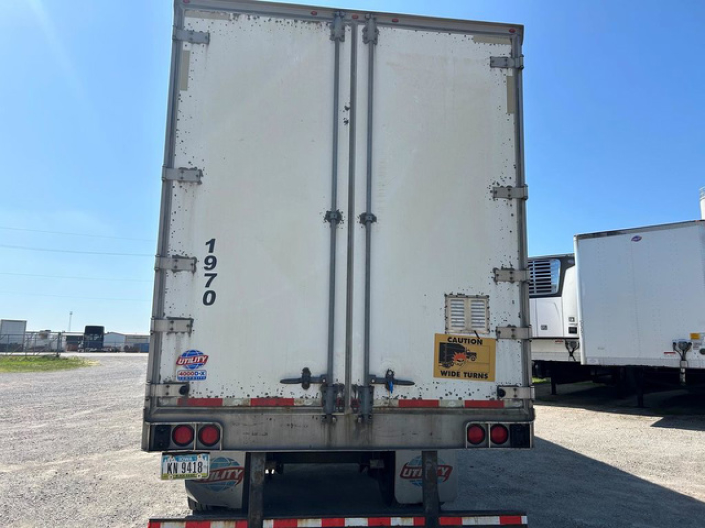 Rear view of a utility van trailer with double doors, vertical reinforcement bars, and bumper lights.