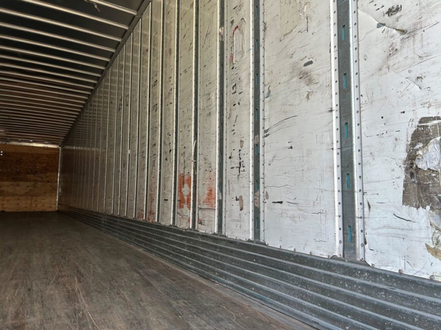 Trailer interior showing metal side walls and wooden floor with scuffed lower edge along the trailer wall.