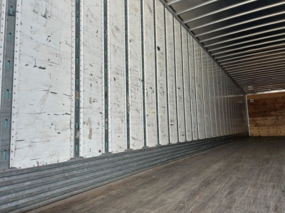 Van trailer interior showing metal wall panels and wooden floor with metal strip rails.