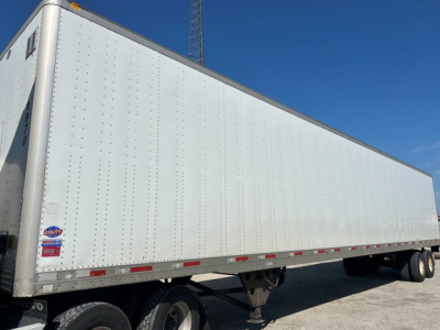Box-style utility van trailer with white riveted aluminum sides and tandem axle, side view showing wheel fenders and rear underride; no visible branding text.