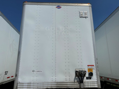 Rear view of a white utility trailer showing a small vent, rear doors, and bumper area with a Coupler/lock mechanism and safety sticker.