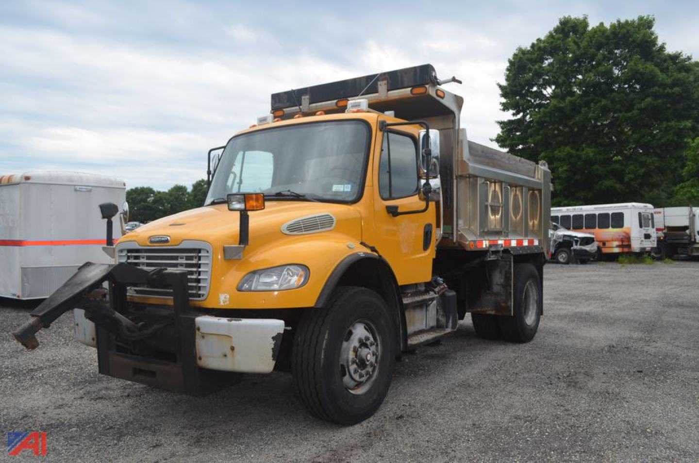 Dump truck in yellow Freightliner M2 106 with dump bed and front bumper guard, side mirrors, and roof lights visible in a lot.