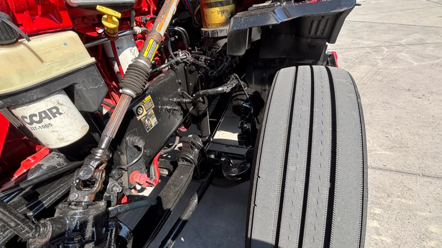 Kenworth T680 chassis showing front suspension and steering components with tire, engine bay area, and reservoir caps visible.
