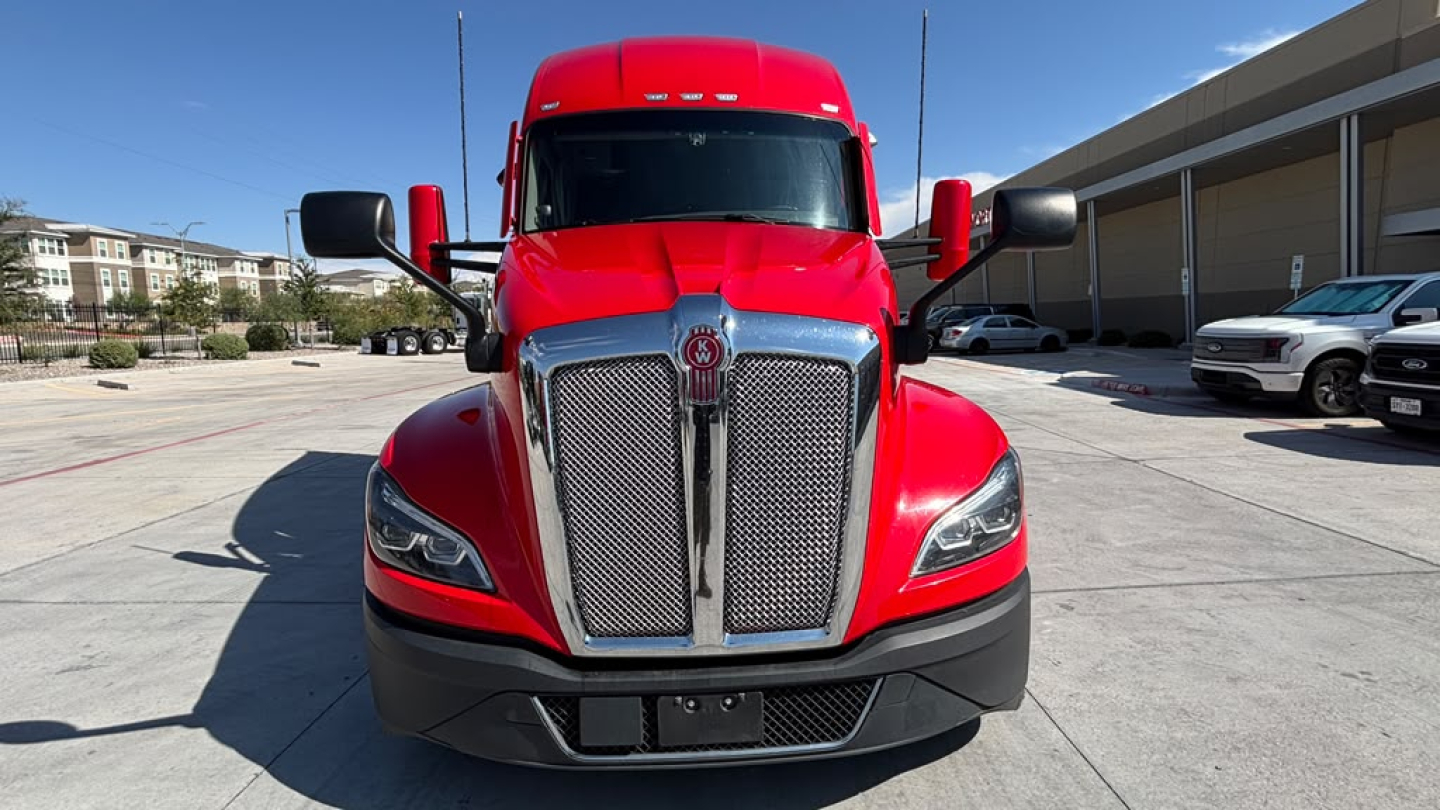 Front view of a red 2023 Kenworth T680 truck showing grille, headlights, and bumper.