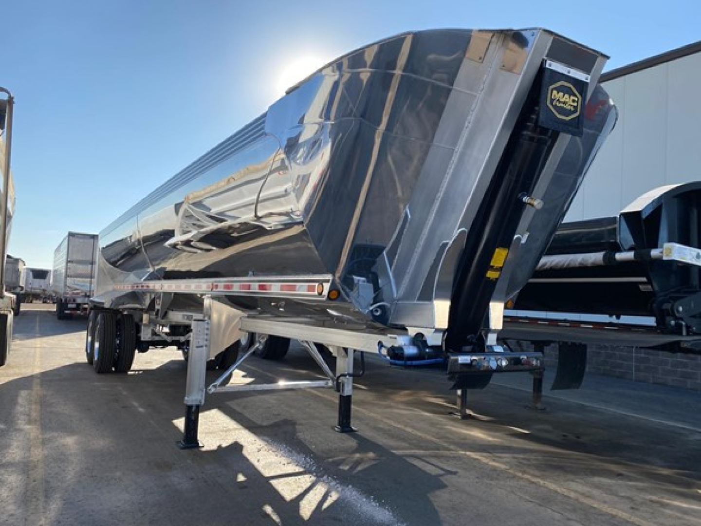 Trailer side showing large metallic end-dump with Mac logo, chrome finish, and black front panel with hitch; appears new Macsimiser 1/2 round aluminum end dump with air ride.