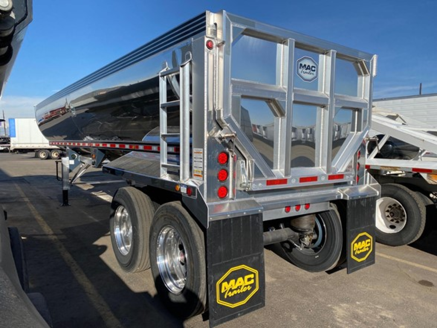 Macsimer 1/2 round dump trailer showing polished aluminum body, dual rear doors, MAC Tools logo bumper, dual axles with chrome wheels, and mud flaps.