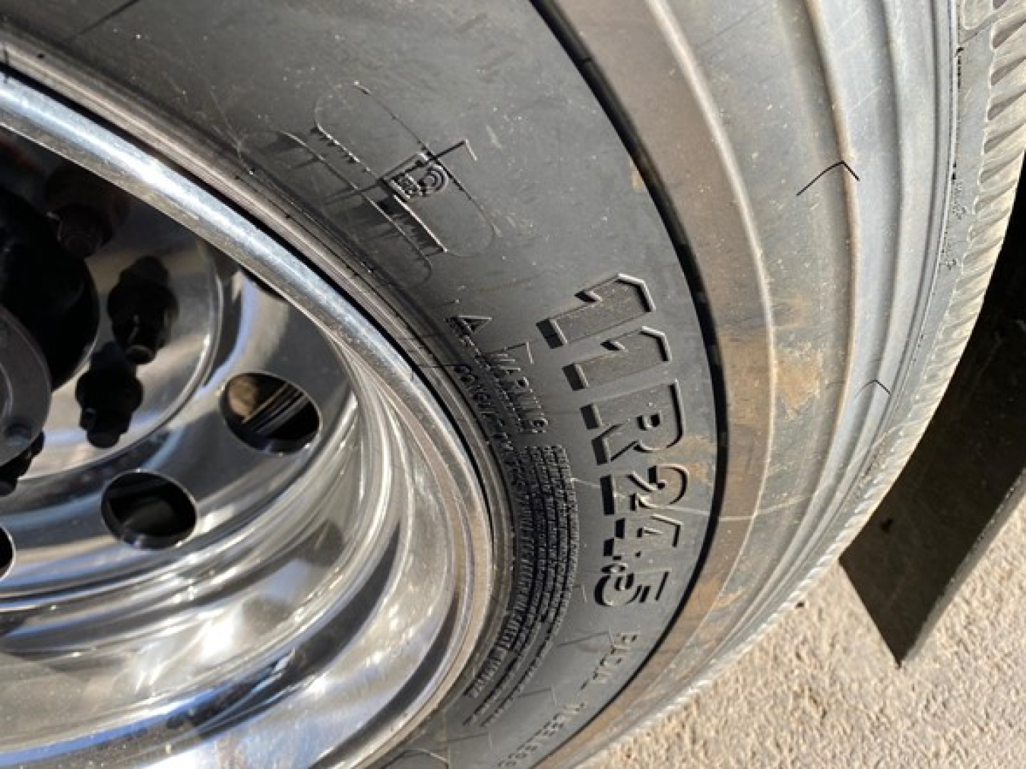 Trailer wheel and tire with visible tire sidewall markings in a dump trailer wheel area.