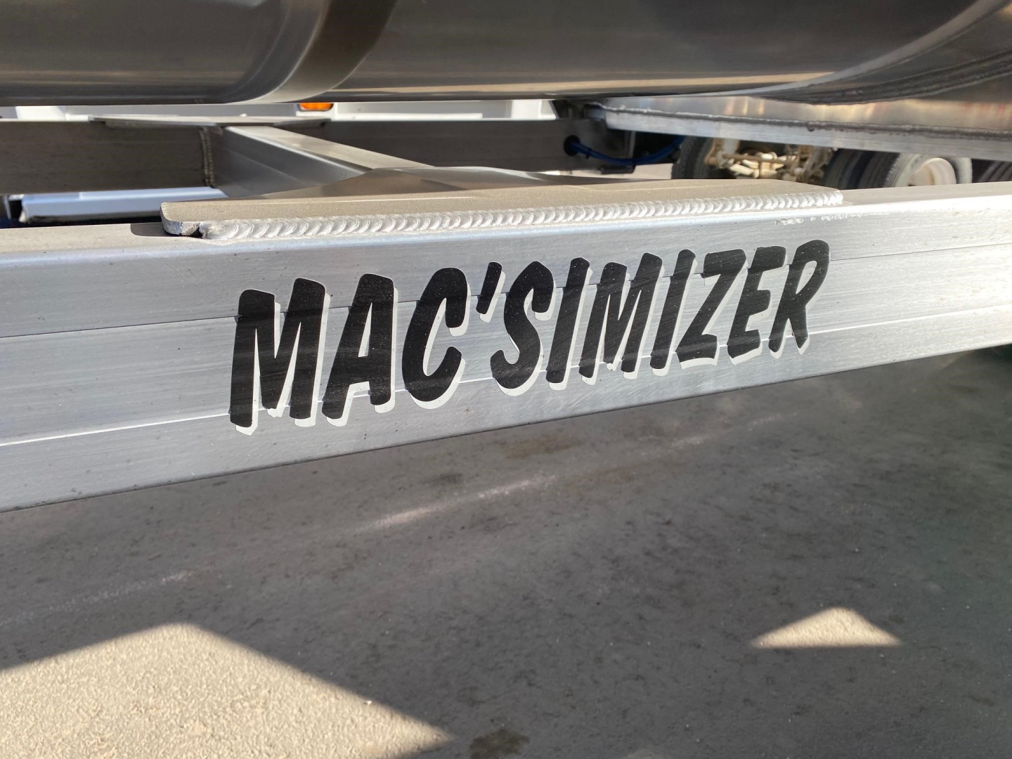 Close-up of a metal trailer frame with the word MAC'SIMIZER in bold black letters along the side.