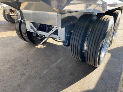 Trailer underside showing dual and triple axle setup with heavy-duty steel frame and wheels, near-ground view.