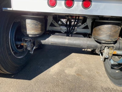 Trailer rear view showing black cylindrical axle housing and dual rear wheels with suspensions under a MacMacsimiser 1/2 round alum end dump. Visible axles, tires, and undercarriage components.