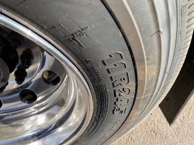 Trailer wheel and tire with visible tire sidewall markings in a dump trailer wheel area.