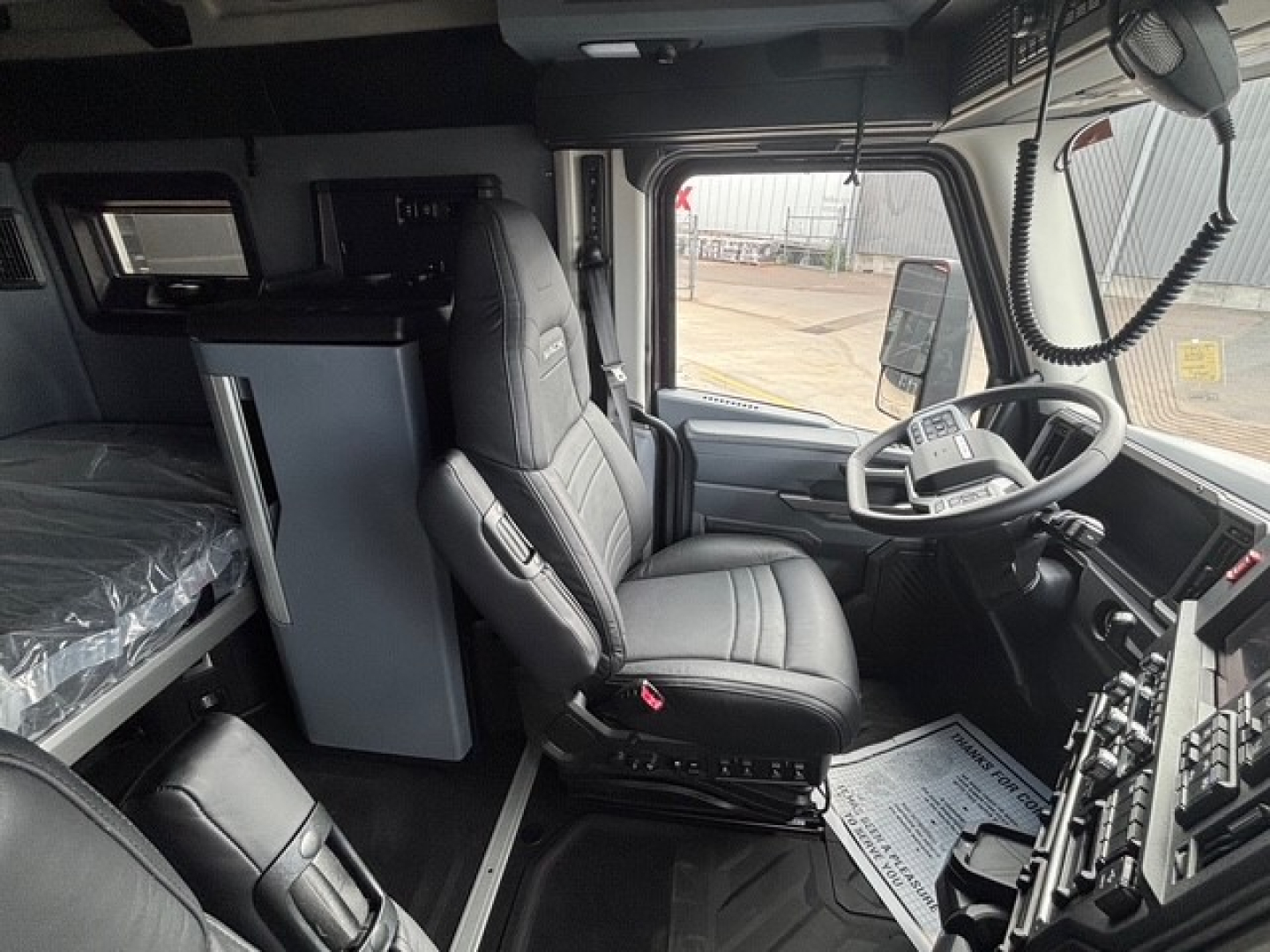 Truck cab interior of a new 2026 Mack PR64T76H tractor showing driver seat, passenger seat, steering wheel, dashboard, and bunk area.
