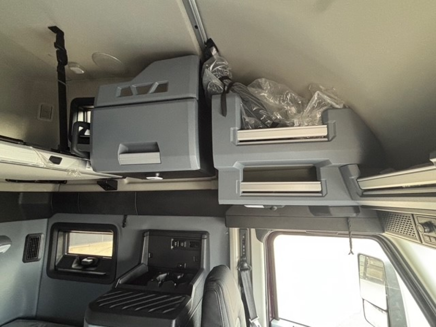 Interior of a Mack PR64T76H cab showing overhead sleeper compartments and storage drawers with plastic wrapping.