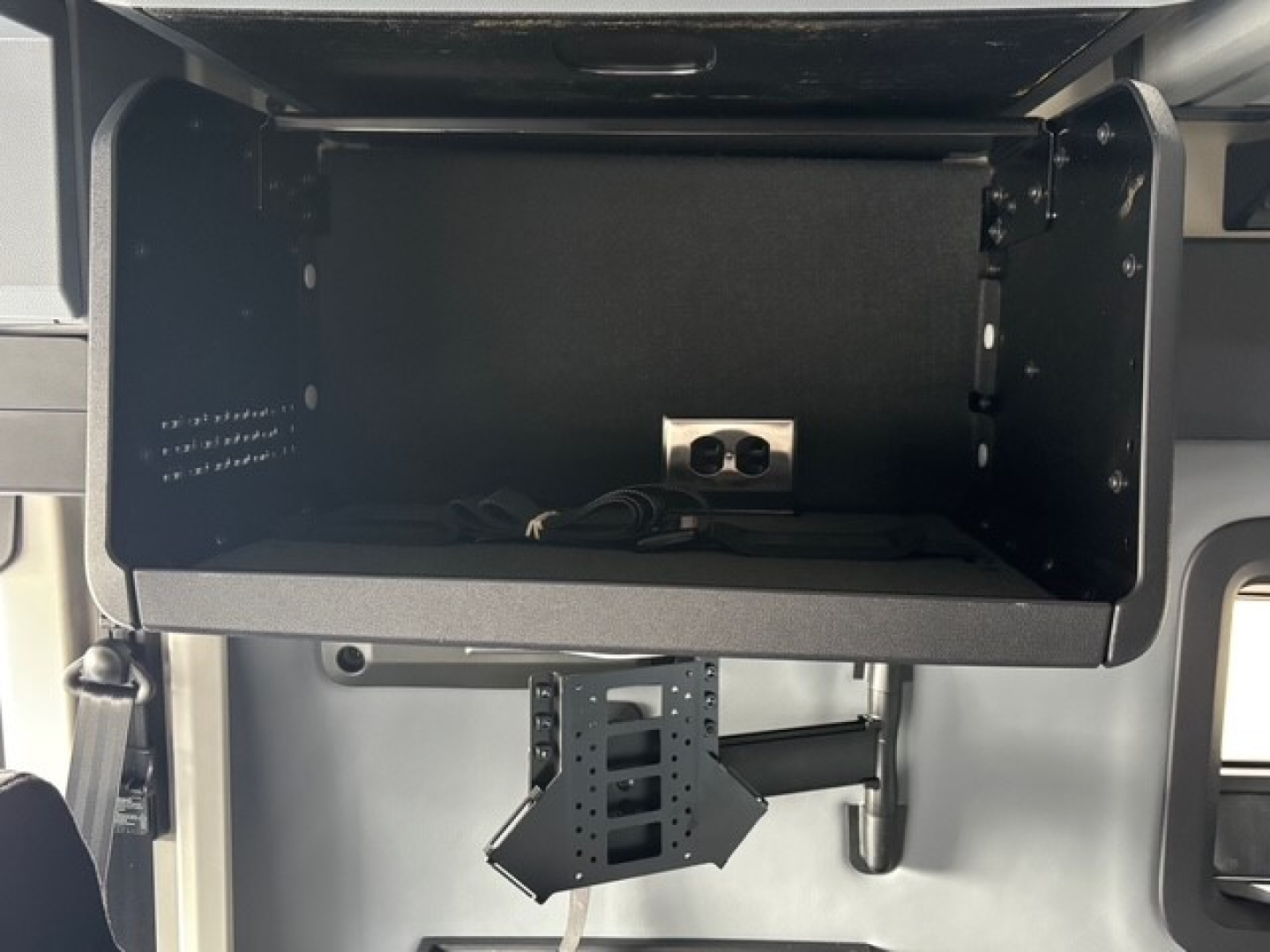 Truck cab interior storage compartment with electrical outlet and mounting bracket visible in the open overhead storage area.