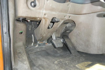 Truck cab interior floor with accelerator and brake pedals; dirt on dashboard area and pedal assembly visible.