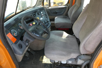 Cab interior of 2017 Freightliner Cascadia 125 daycab showing steering wheel dashboard gauges and gray cloth seats.