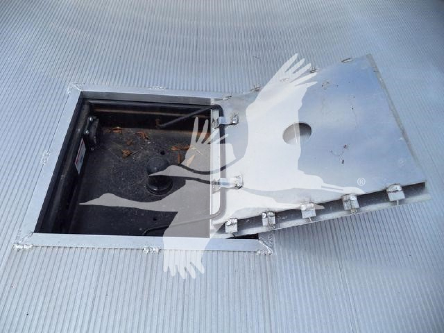 Vehicle storage hatch cutout in truck bed lid showing opening inside with black interior and hinges.