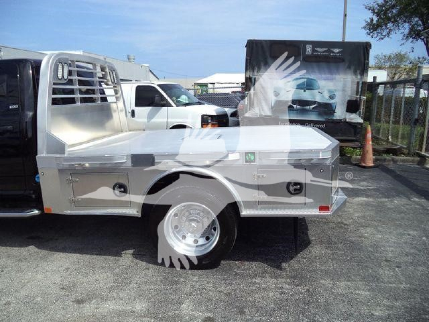 Ram 5500 flatbed truck side view showing aluminum flatbed with wheel, cabin ladder rack, and stock trailer in background.