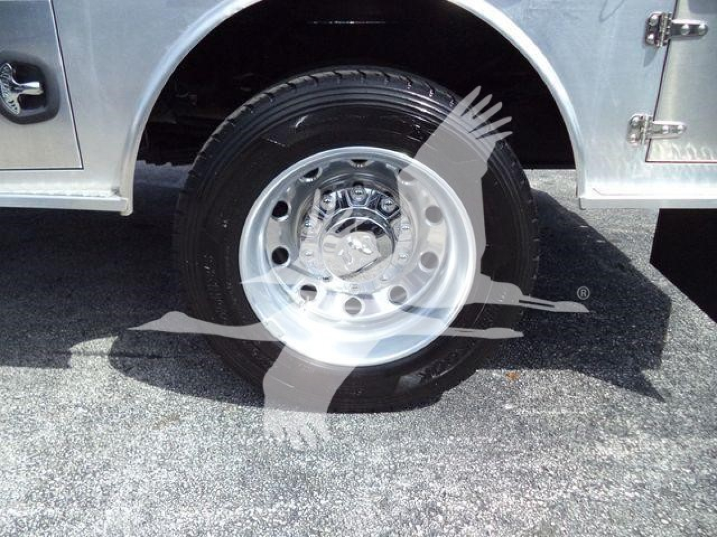 Wheel and tire assembly of a RAM flatbed truck showing a polished steel wheel with lug nuts and a black tire; part of a chrome-finished body panel is visible.