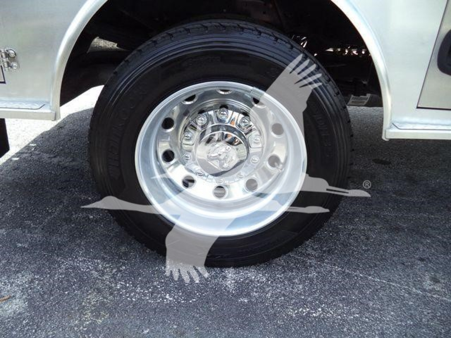 Truck wheel and tire assembly showing polished steel rim and black tire in front of a flatbed truck fender.