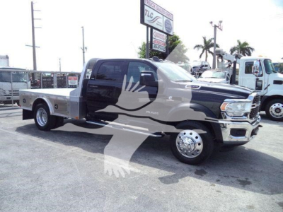 Ram 5500 flatbed truck in showroom lot showing side profile and dual rear wheels, Crew Cab, chrome front bumper, large side mirrors, flatbed rear.