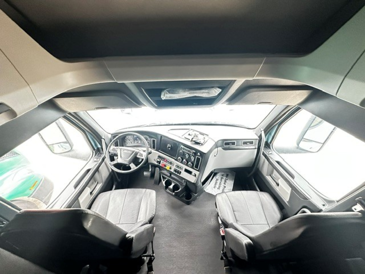 Cab view of a 2023 Freightliner Cascadia 126 conventional sleeper showing dashboard, steering wheel, and two captain seats.