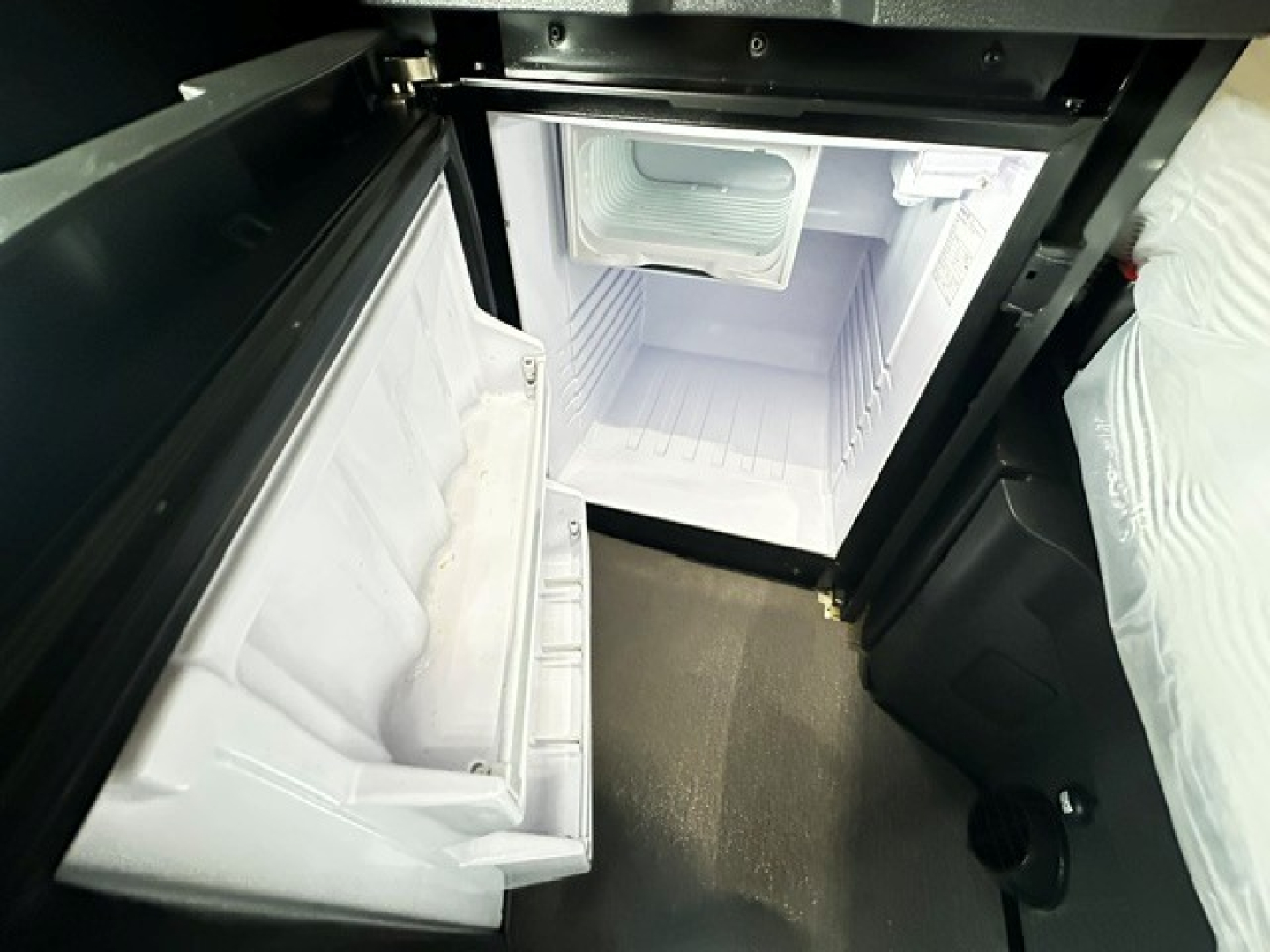 Freightliner Cascadia 126 sleeper cab interior with open under-bunk storage chest and small refrigerator in top compartment.