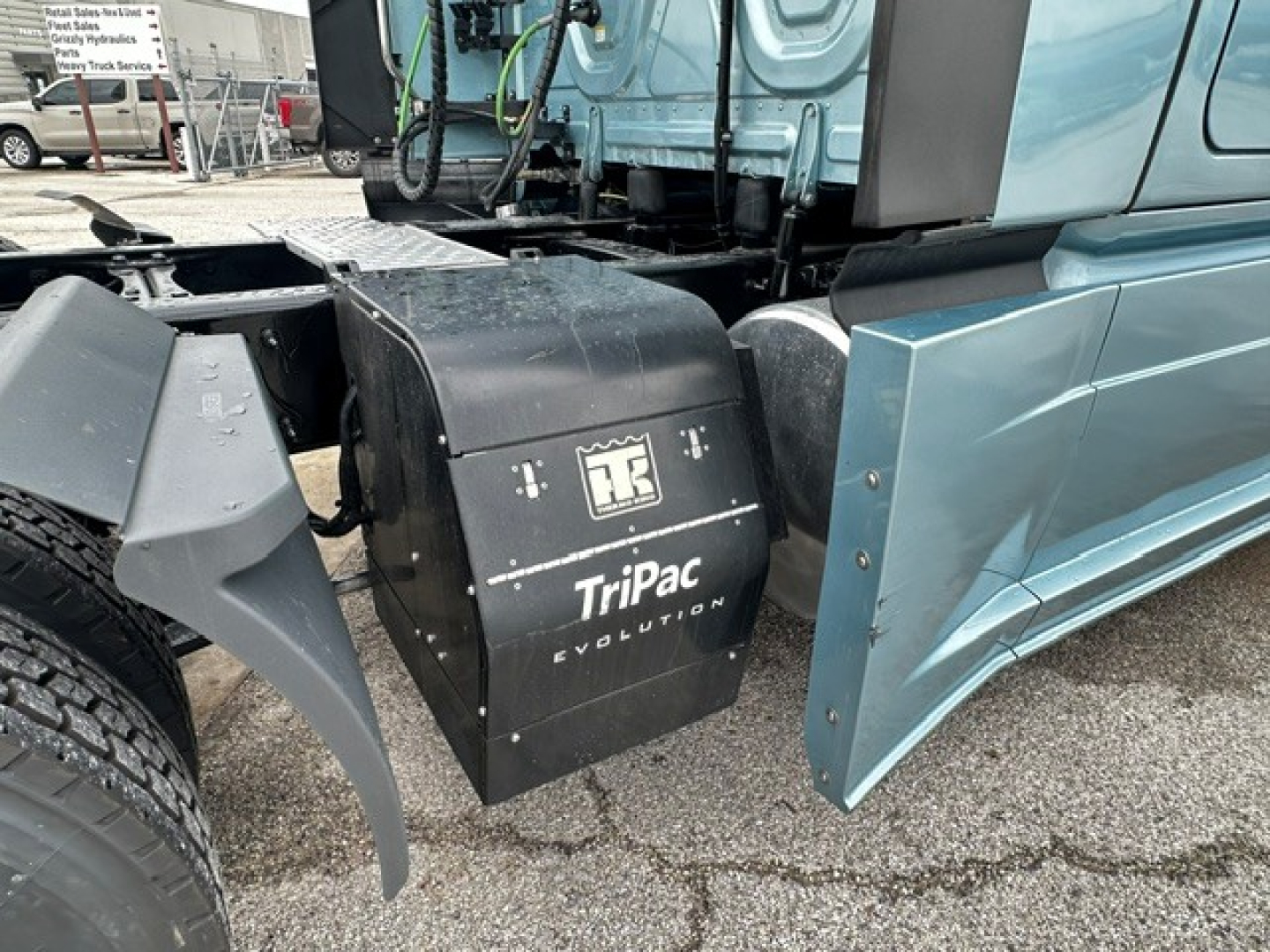 Truck side view showing black rectangular TriPac Evolution auxiliary power unit mounted behind cab on a blue Freightliner Cascadia 126.