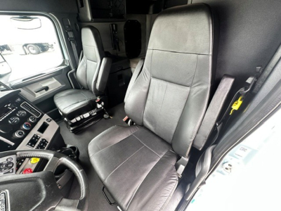 Truck cockpit interior with driver and passenger seats in a Freightliner Cascadia cab, dashboard controls visible on left side.