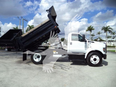 Dump truck in-service 2017 Ford F650 with dump bed raised, side profile, white cab, black dump body, highway surroundings.