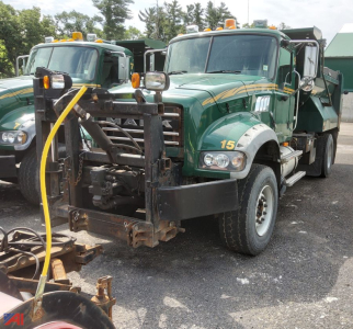 Mack Granite dump truck with plow attachment visible from front-left view; green cab with yellow stripes and number 15, dual headlights, plow frame, and side mirrors.