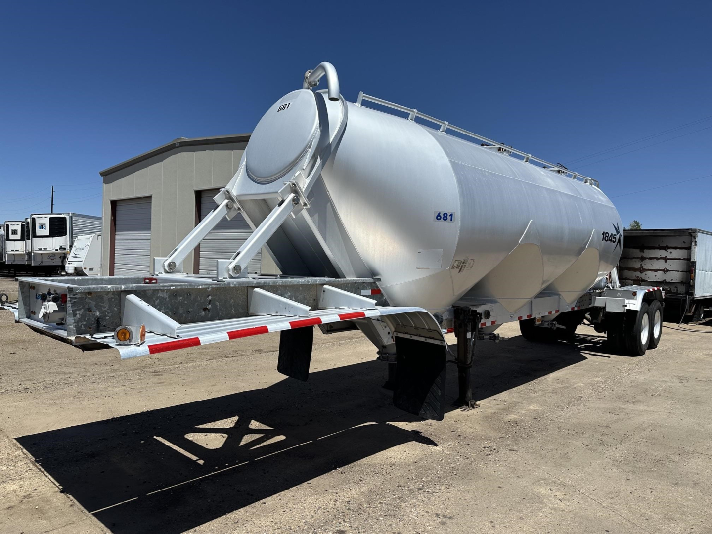Polyethylene tank trailer for dry bulk with rear gravity drop pneumatic system, 3-hop air ride suspension, cylindrical stainless tank, front ladder structure, side access manway, treaded landing gear, blue sky.