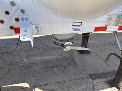 Trailer undercarriage showing landing gear and axles with a round air ride component, wheels, and a small label on the side of the tank.