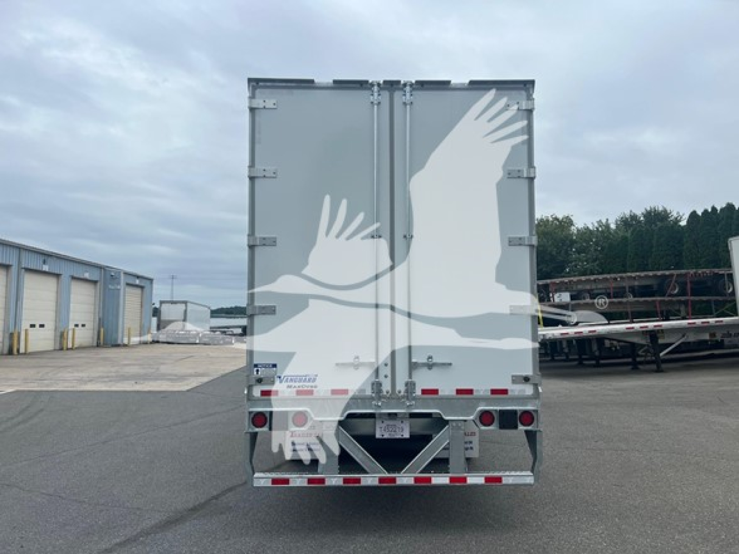 Rear view of a Vanguard sheet/post trailer with a graphic of two white birds in flight on gray doors, reflective tape along bottom edge, and license plate area in center.