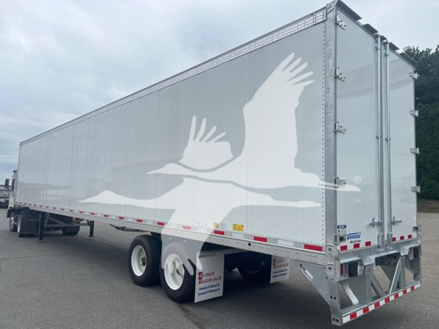 Trailer side view showing large silver box trailer with white gull logo and rear doors, aluminum frame, dual rear axles, wheel fenders, VM605644 stock tag.