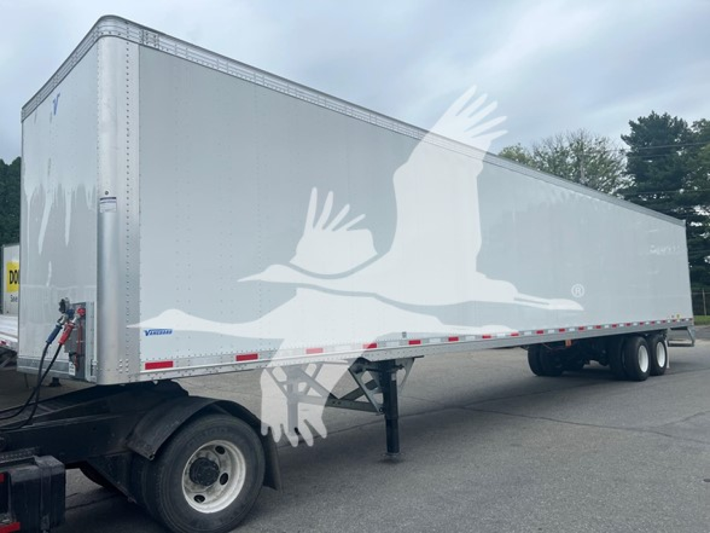 Trailer side view showing large white graphic of a bird and wings along a Vanguard-style sheet trailer with silver body and red/white reflective trim.