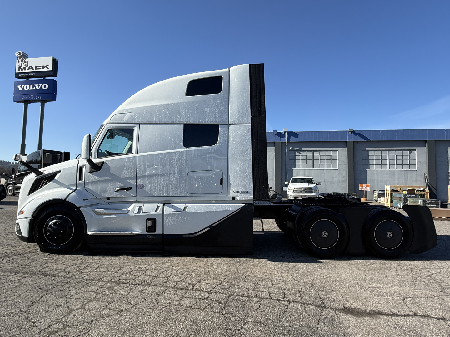 Volvo VNL64T860 truck side view showing sleeper cab and flatbed rear with triple rear axles.