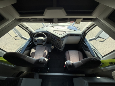 Cab interior of a Volvo VNL truck showing driver and passenger seats, steering wheel, dashboard, and large windshield from a high angle.
