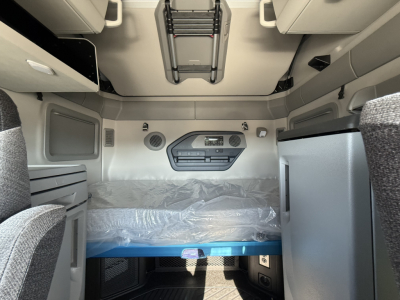 Interior of Volvo VNL64T860 sleeper cab showing bunk area with mattress wrapped in plastic, overhead storage, and control panel on bulkhead.