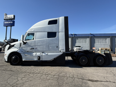 Volvo VNL64T860 truck side view showing sleeper cab and flatbed rear with triple rear axles.