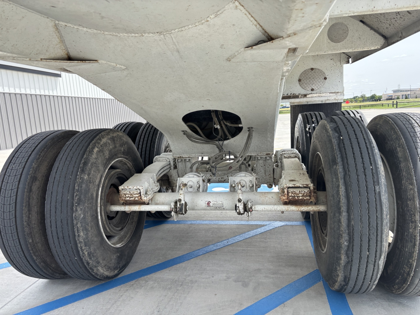 Trailer axles and undercarriage showing dual rear axles with leaf-spring suspension and tires, underside view of dump trailer.