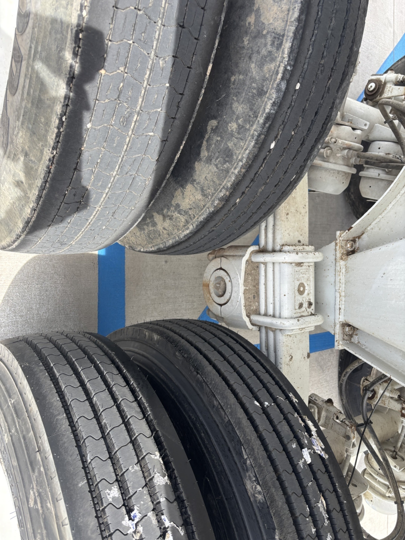 Truck trailer wheels and suspension components showing dual rear tires with tread, metal axles, and hydraulic suspension linkage.