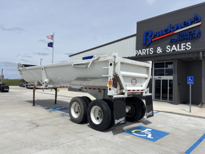 Dump trailer in service position showing triple-axle rear with white paint, Bruckners Parts & Sales building in background, handicap parking. Visible text on trailer mudflaps and equipment: none legible; building signage reads Bruckners Par