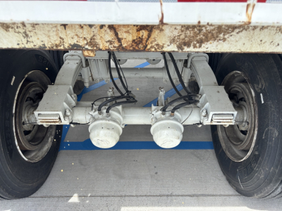 Dump trailer underside showing dual axles with leaf springs and hubs, wiring harnesses, and suspension components.