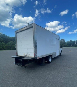 Box truck from rear-left angle showing a white box body on a Ford E-Series Cutaway cab; open lift gate and cargo area visible.