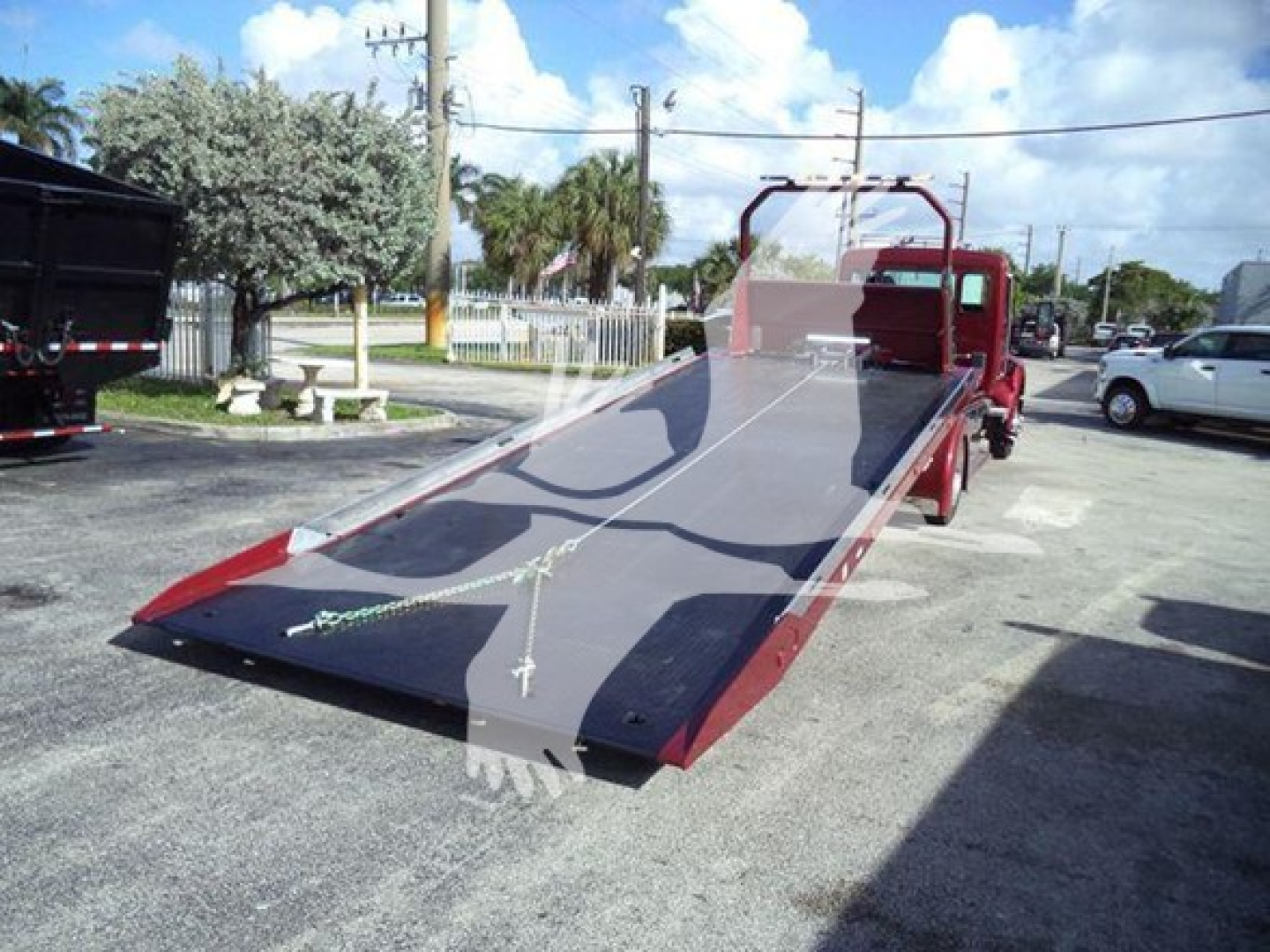 Truck roll-back flatbed with a red cab and parked in a lot. Flatbed surface visible with slight reflection and overhead power lines.