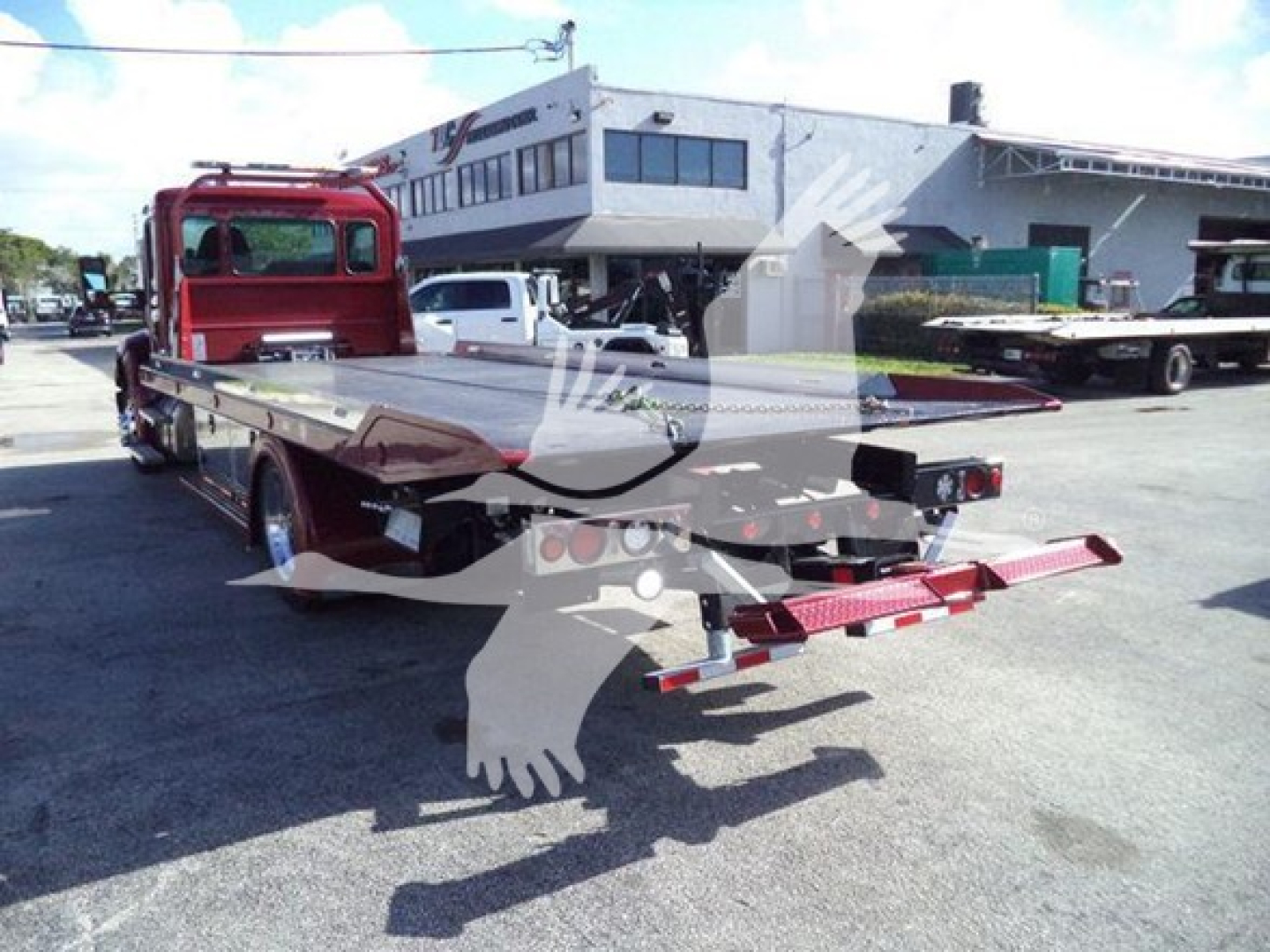 Kenworth T680 rollback tow truck flatbed with red cab and long loading bed; rear view shows tow equipment and warning stripes; VIN/stock not visible on text.
