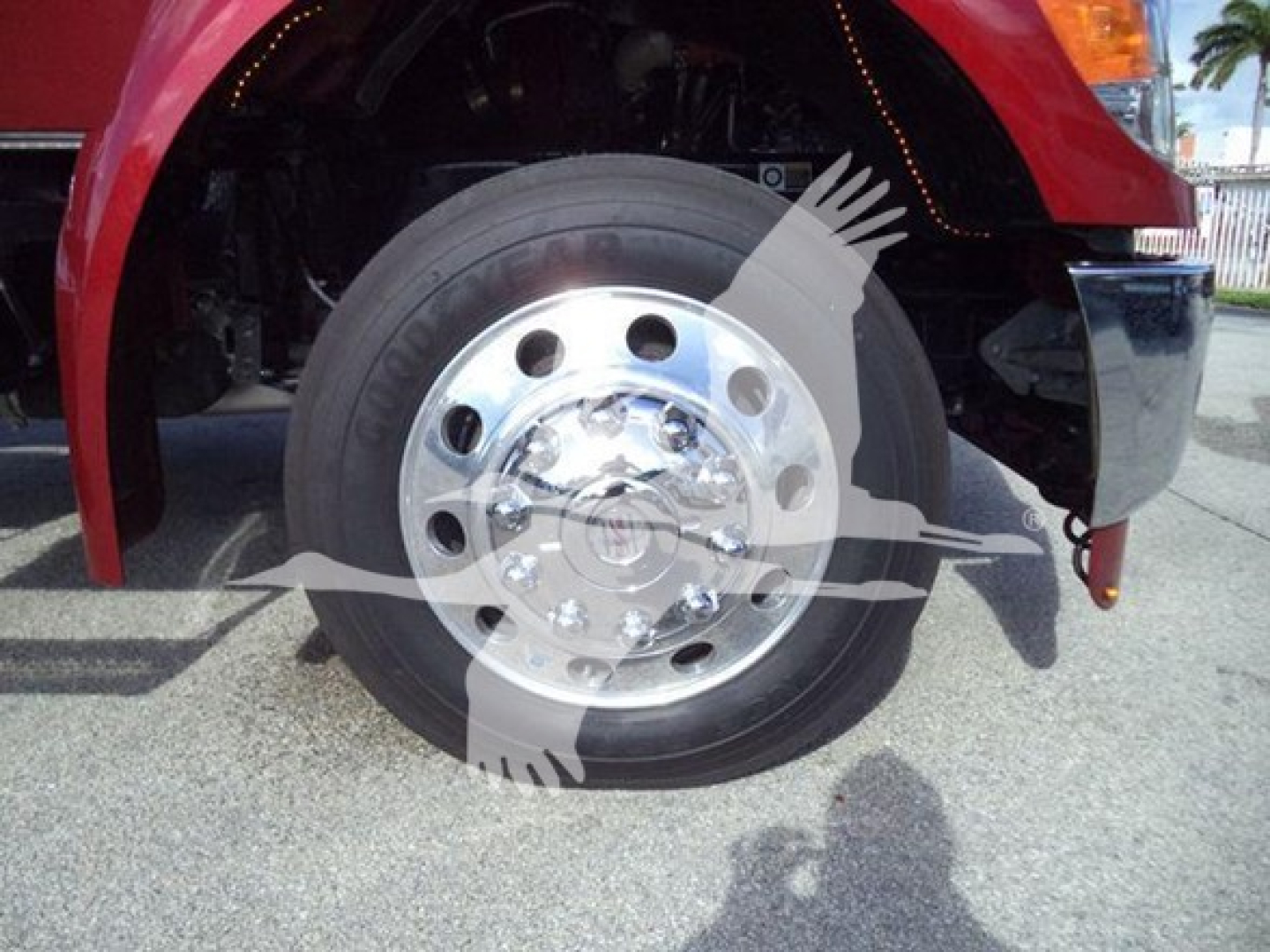 Kenworth truck wheel and front fender with chrome hubcap and black tire, red body panel visible.