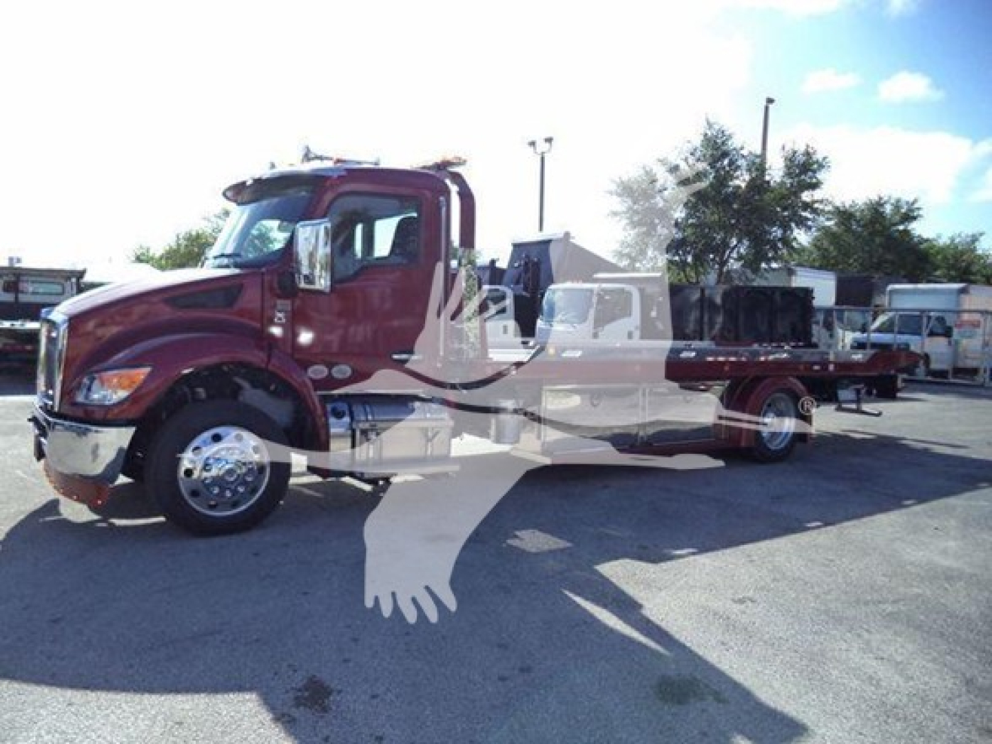 Kenworth T280 rollback truck in a parking lot with chrome wheels and burgundy cab; side text or decals faintly visible on the door and long chrome exhaust; landscape orientation.